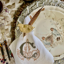Load image into Gallery viewer, Decorative table setting with a napkin featuring a monogram, a plate with bird design, and a gold leaf.