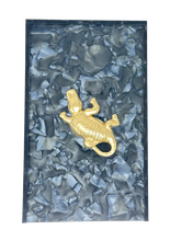 Load image into Gallery viewer, Gold alligator pendant on a textured blue background
