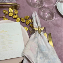 Load image into Gallery viewer, Elegant table setting with gold leaves, white napkin, and floral decorations on a purple tablecloth.
