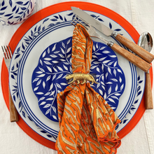 Load image into Gallery viewer, Decorative table setting with a blue and white plate, orange napkin, and cutlery on a white tablecloth.
